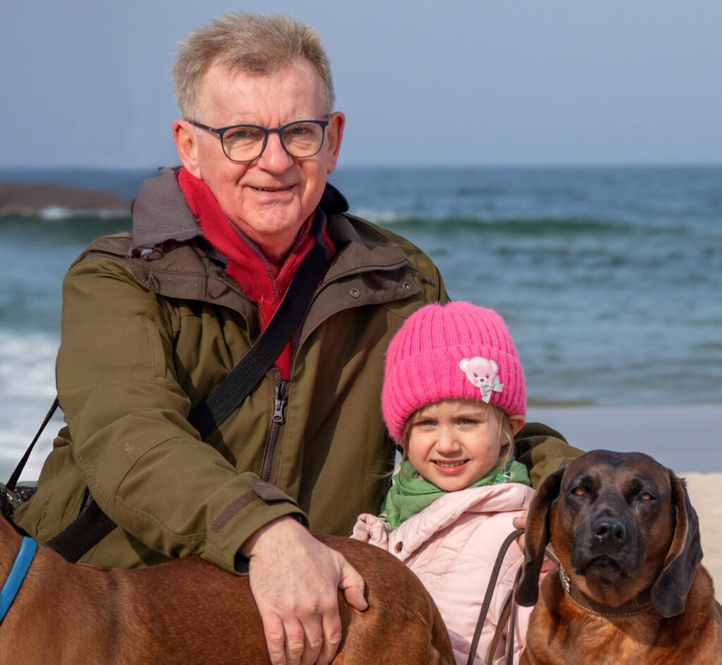 Ein aelterer Mann und ein Kind mit einem Hund am Strand von Wolin.